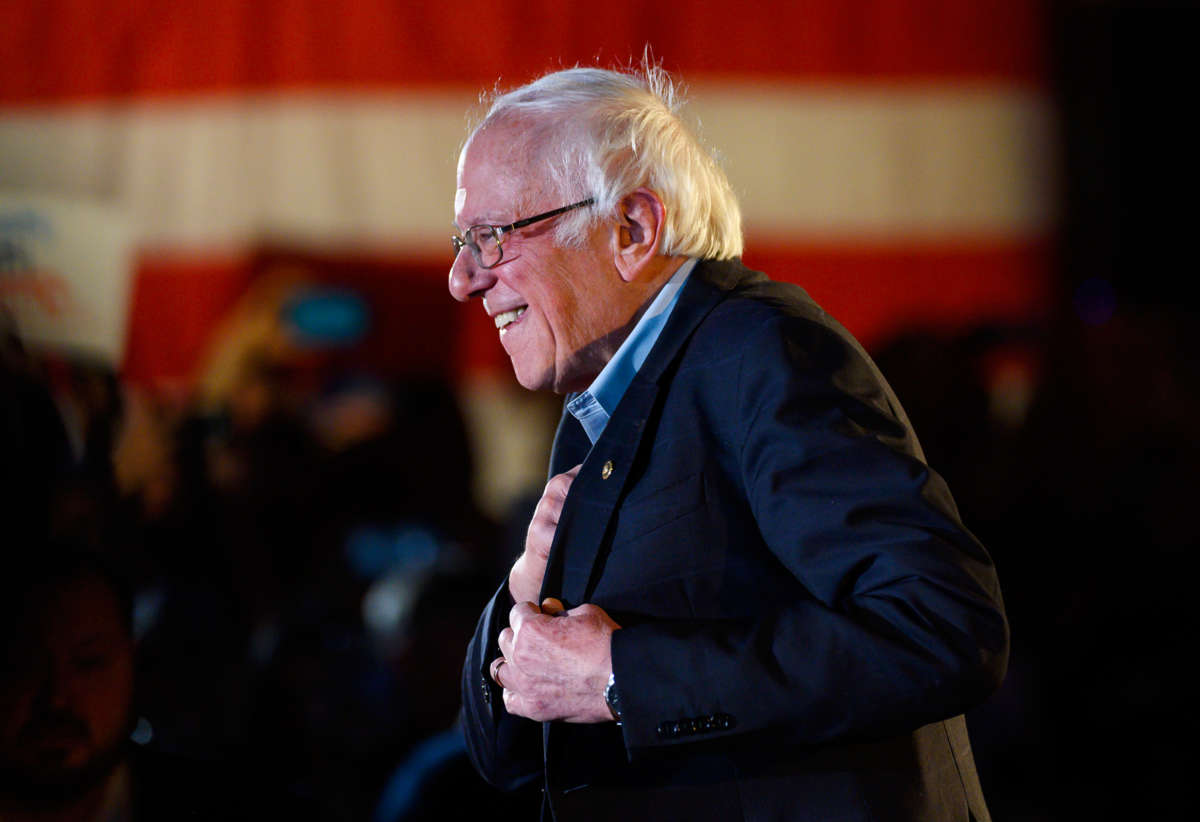 Bernie Sanders stands at a podium and smiles at a crowd of his supporters