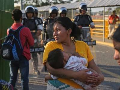 A woman holds her baby while police stand behind her