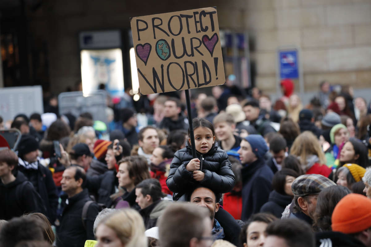 A child carries a sign reading "PROTECT OUR WORLD" during a protest