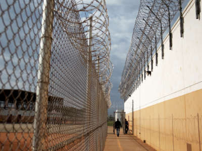 A guard walks down a barbed-wired corridor