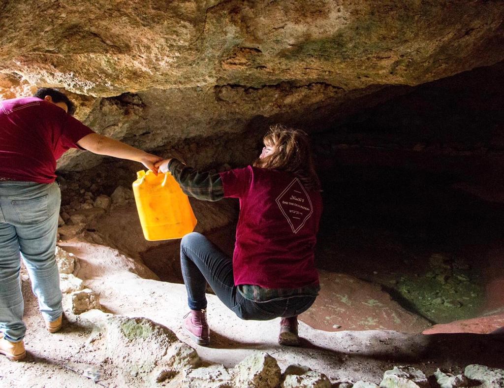 A woman passes a jug of water to another person while in a cave