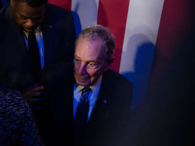 Mike Bloomberg stands in front of a U.S. flag flanked by supporters