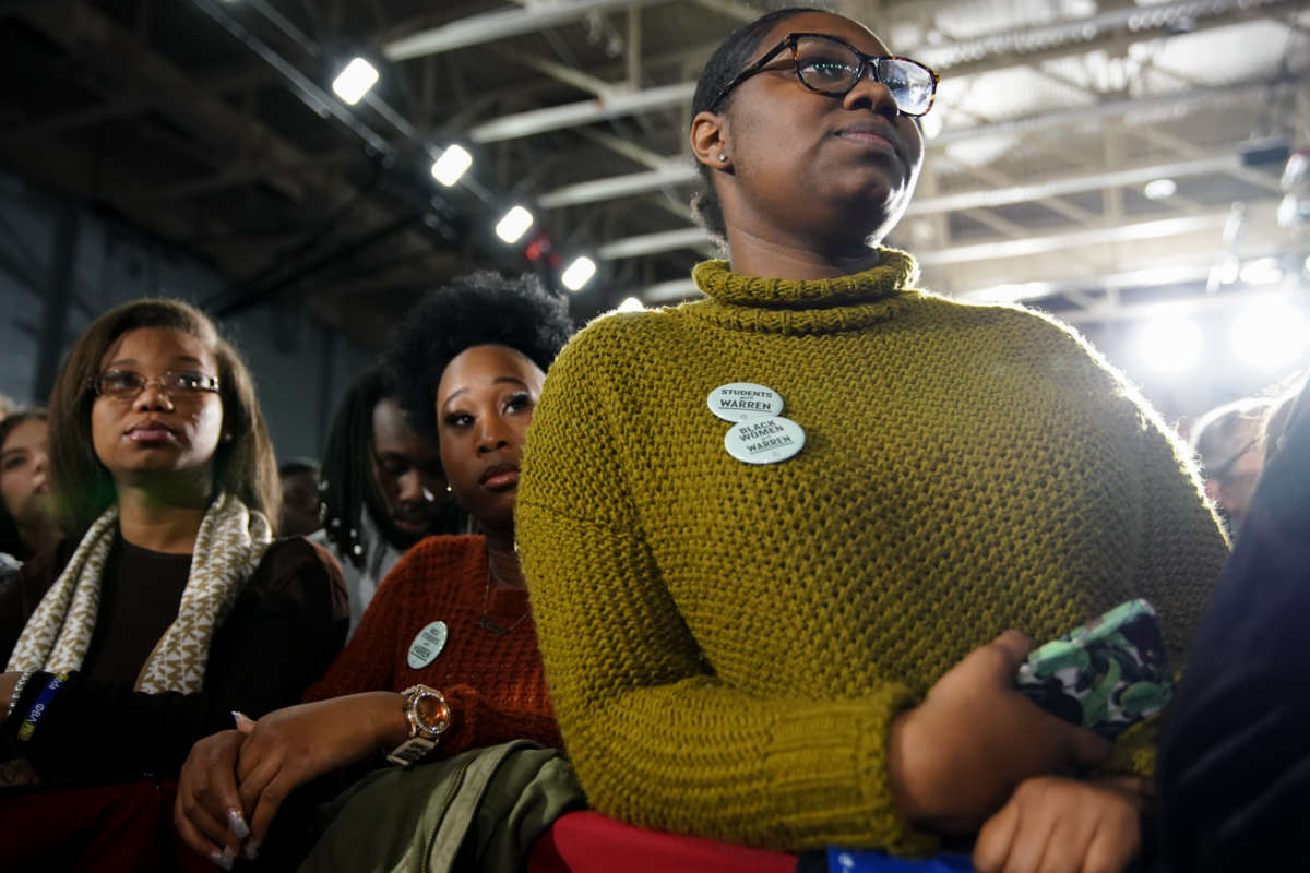 Black women wearing pro-Warren pins listen during a campaign event