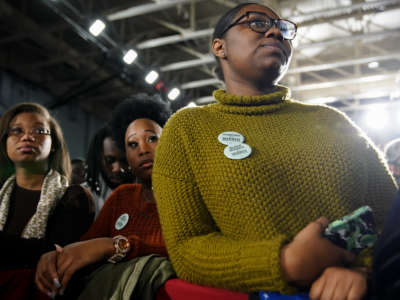 Black women wearing pro-Warren pins listen during a campaign event