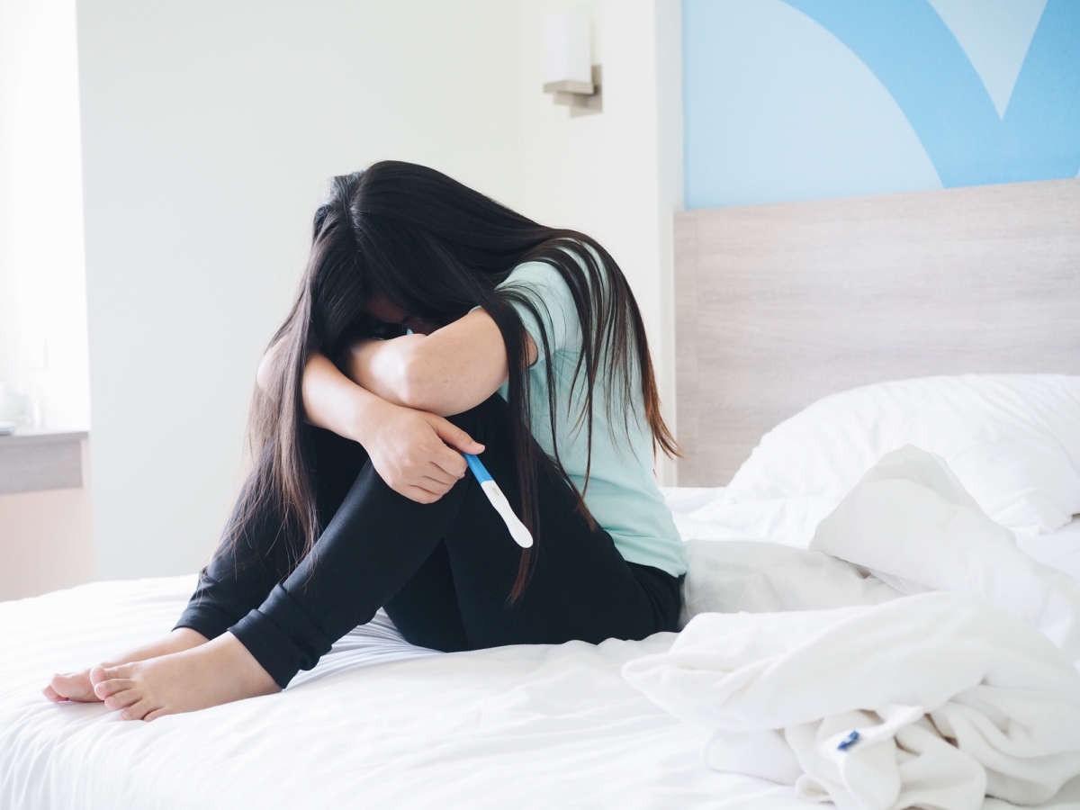 A woman hides her face in sorrow while holding a pregnancy test