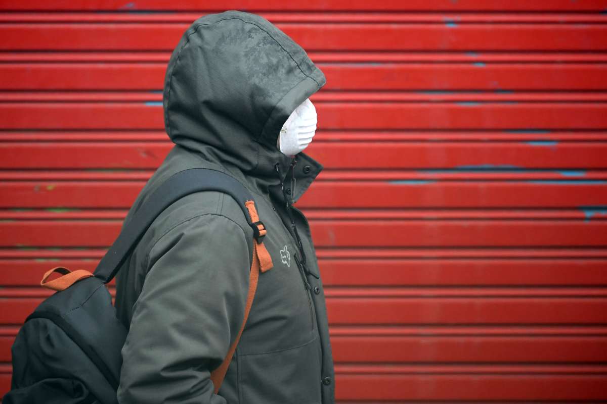 A person walks by a red wall wearing a face mask