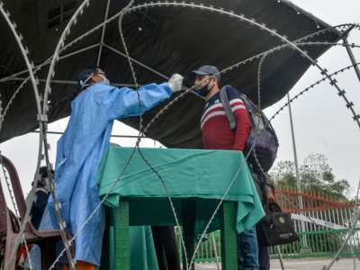 Health workers check the body temperature of an Indian national coming from Bangladesh, following an announcement about the closure of the India-Bangladesh border as a preventive measure against the spread of the COVID-19 coronavirus, at Fulbari Border checkpoint, on March 13, 2020.