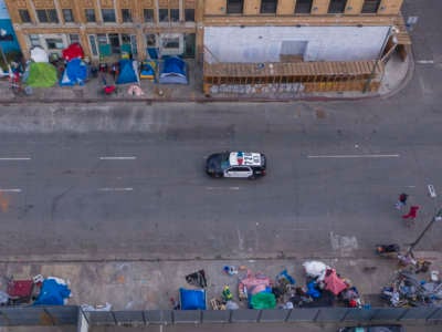 A police car passes homeless people on Skid Row after the new restrictions went into effect as the coronavirus pandemic spreads on March 20, 2020, in Los Angeles, California.