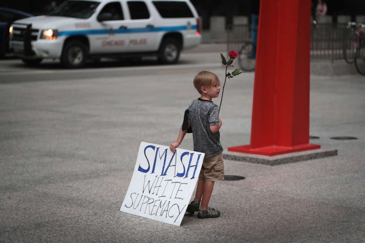 A young boy holds a sign reading "SMASH WHITE SUPREMACY" in one hand and a rose in the other during a protest