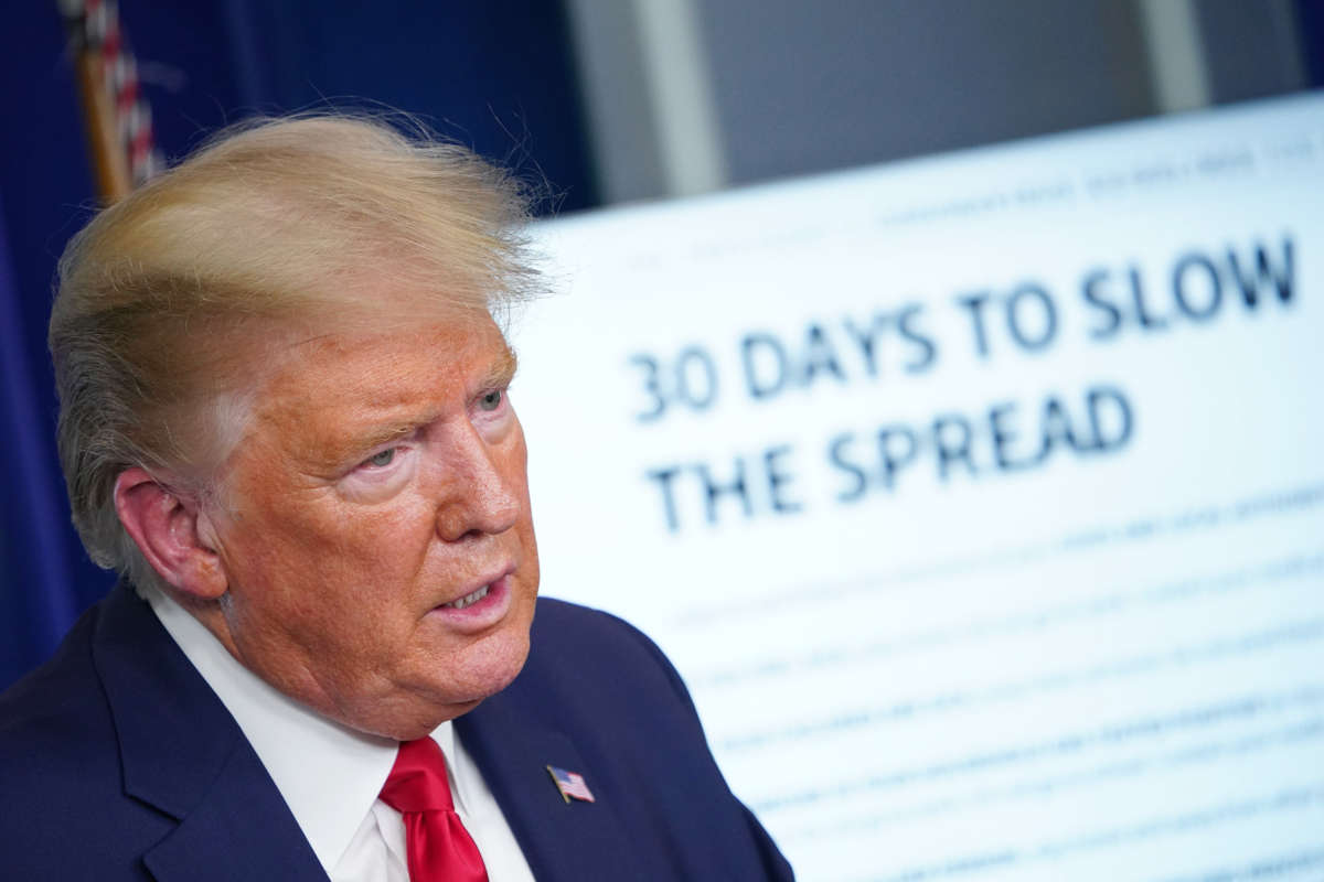 Donald Trump stands in front of a display reading "30 DAYS TO SLOW THE SPREAD"