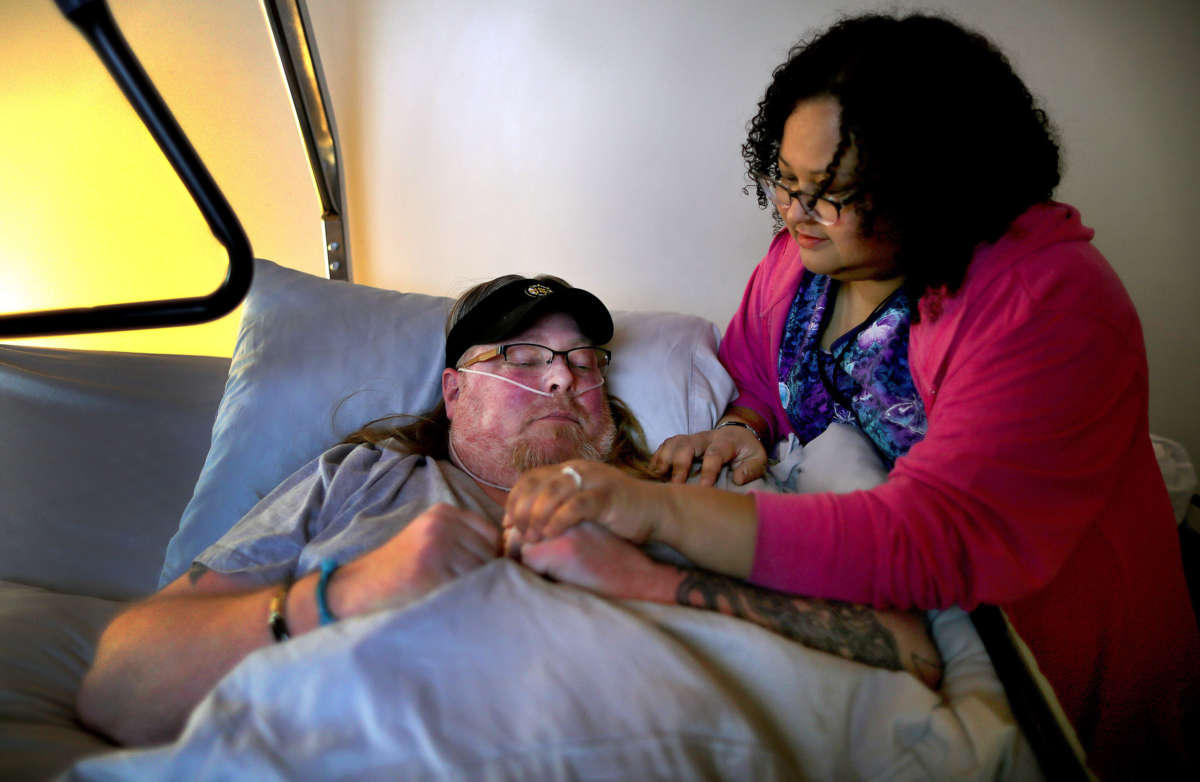 Melissa Baptista checks on her fiancé Eric McGuire, who is bedridden with several medical conditions and is on oxygen, in Franklin, Massachusetts, on March 25, 2020. Melissa is a nurse at a nearby nursing home and depends on caregivers to take care of his needs, but one caregiver plans to isolate herself because she has a sinus infection and will be tested for coronavirus.