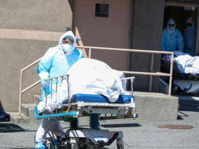 Health officials carry the body of a COVID-19 victim on a stretcher to container morgues by the Wyckoff Heights Medical Center in Brooklyn, New York City, on April 6, 2020.