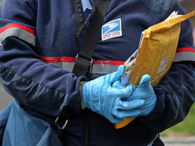 A USPS postal worker wears protective gloves while making deliveries in Cambridge, Massachussetts, during the COVID-19 pandemic on April 8, 2020.