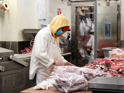 A worker handles meat in a butchery