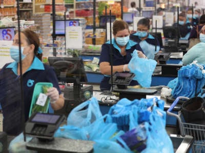 Cashiers stand behind partial protective plastic screens and wear masks and gloves as they work at the Presidente Supermarket on April 13, 2020, in Miami, Florida.