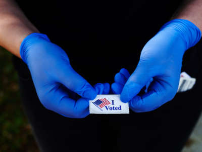 A voter holds an "I Voted" sticker while wearing a pair of rubber gloves after voting in Florida's primary election at the Oldsmar Fire Department voting precinct on March 17, 2020, in Oldsmar, Florida.