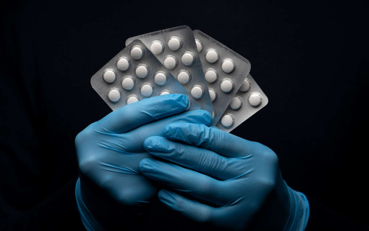 A pack of hydroxychloroquine sulfate medication is held by hands in surgical gloves.
