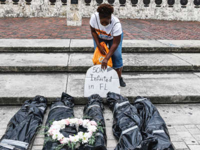 A woman places a fake headstone near also fake bodybags to illustrate the number of covid deaths in Florida