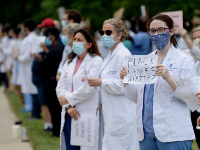 Medical professionals wearing ppe stand during a protest as one displays a sign reading "Black Lives Matter"