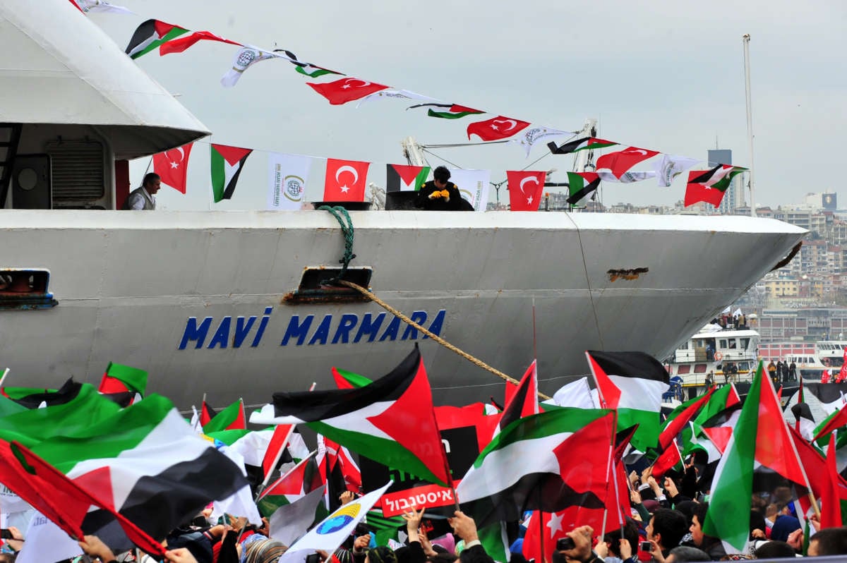 People wave Palestinian and Turkish flags in front of a ship reading "Mavi Marmara"