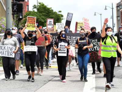 Masked protesters march while holding sineage