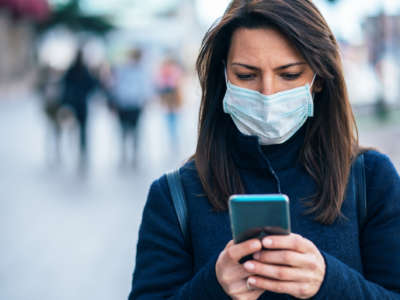 A woman looks at her phone while wearing a facemask outdoors