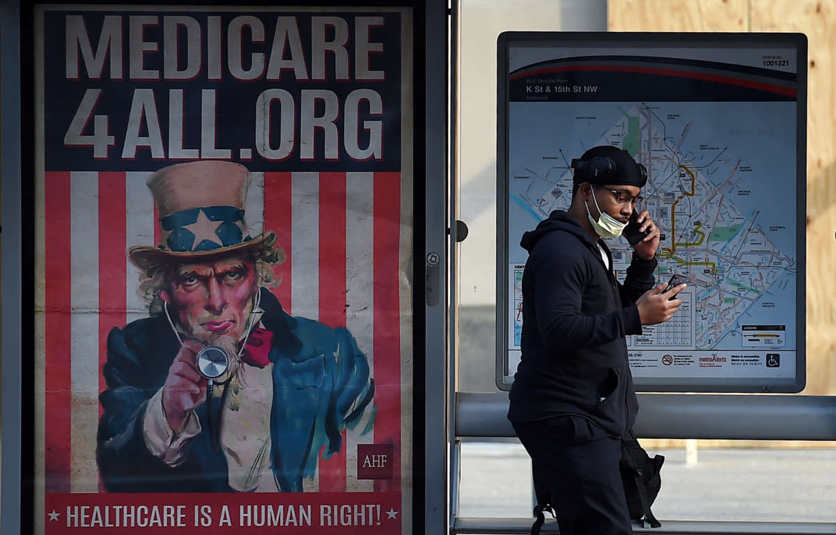 A pedestrian wearing a protective mask checks her phone near as she walks by a Medicare for All bus stop billboard in Washington, D.C., on June 3, 2020.