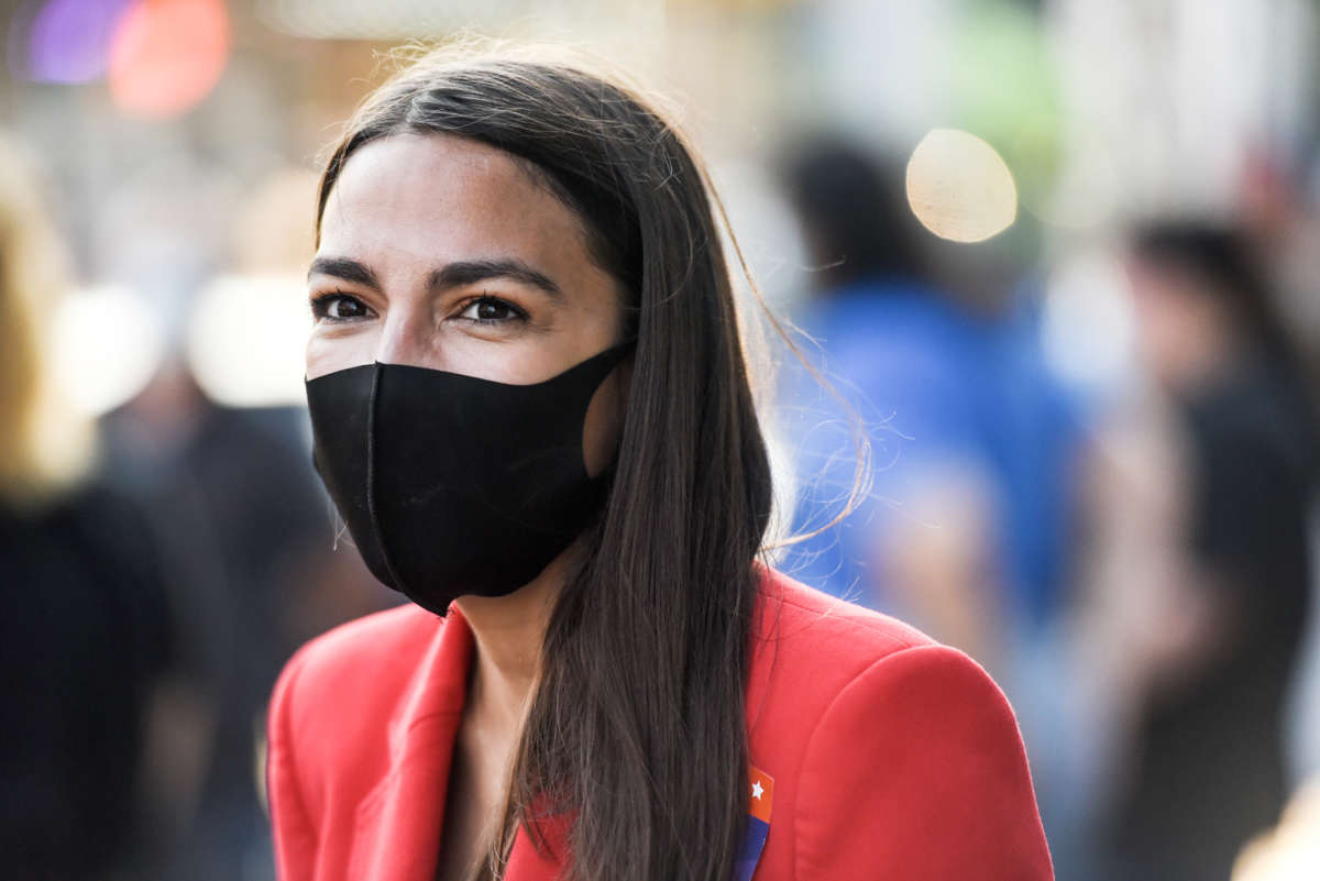 Alexandria Ocasio-Cortez (AOC) smiles from behind a face mask