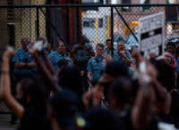 Cops watch people protest from behind a chain link fence