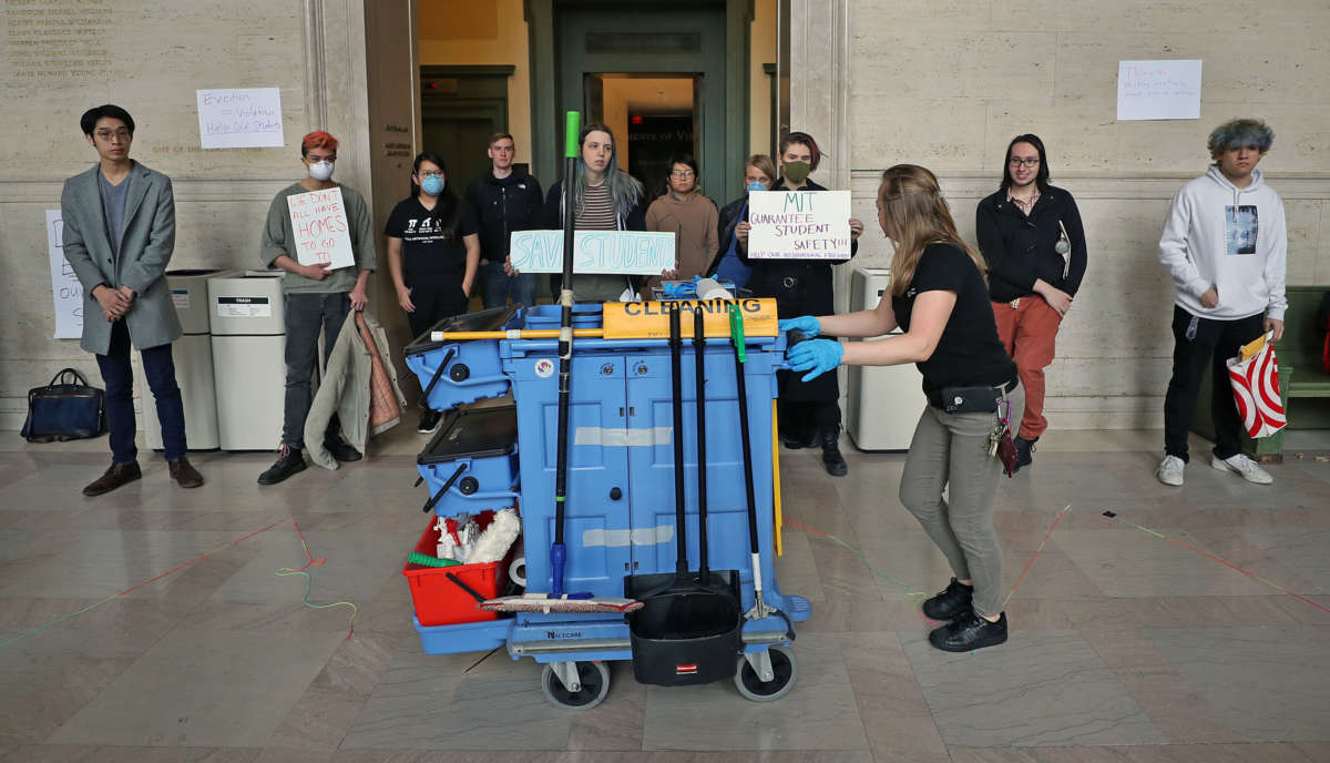 A MIT custodian with her cleaning cart walks past MIT students during an MIT international student demonstration on March 12, 2020, in Cambridge, Massachusetts.