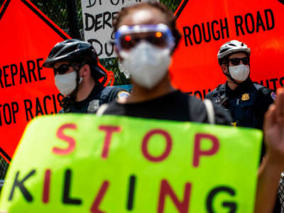 A protester holds a sign that reads "Stop Killing" while standing near policemen during a small standoff between police and protesters in front of Lafayette Square near the White House in Washington, D.C., on July 4, 2020.