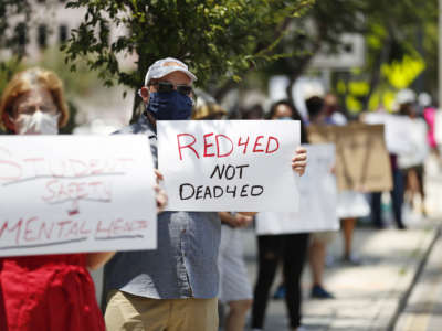 A teacher holds a sign reading "RED 4 ED NOT DEAD 4 ED" during a socially distanced protest