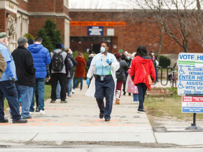 A woman hands out surgical masks to people standing in line to vote in Wisconsin's primary election on April 7, 2020, at Riverside High School in the city of Milwaukee.