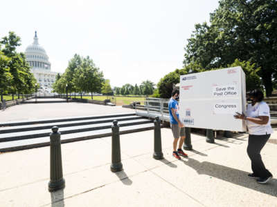 From left, Garrett Schaffel, and Judy Beard, American Postal Workers Union national legislative and political director, carry a Priority Mail box towards the Capitol for a photo-op on Tuesday, June 23, 2020.