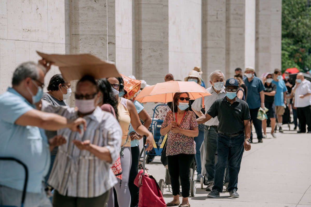 Masked people stand in a line outdoors while waiting for food donations