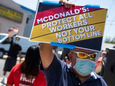 A McDonald's worker holds a sign reading "MCDONALD'S: PROTECT ALL WORKERS NOT YOUR BOTTOM LINE