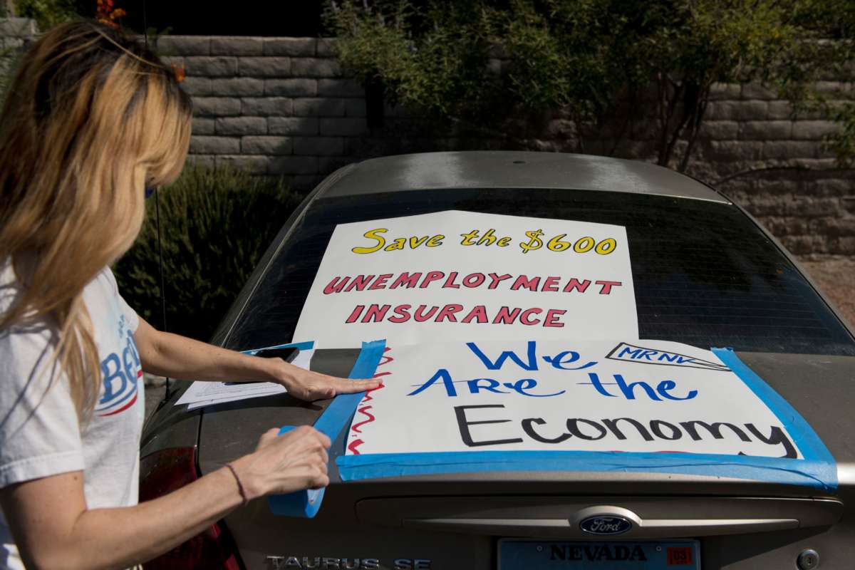 A masked woman tapes signs reading "Save the $600 unemployment insurance" and "We are the economy" to her car