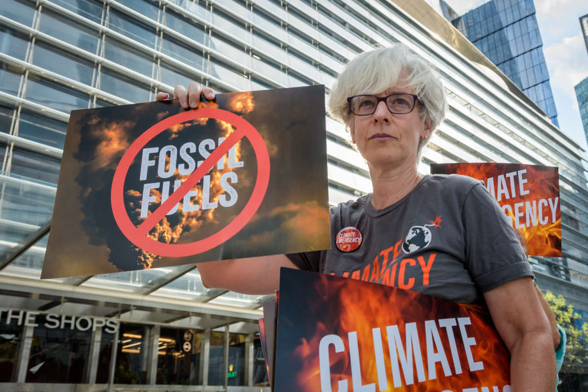 A climate activist holds signs that read "Fossil Fuel" with a large red "no" symbol over it