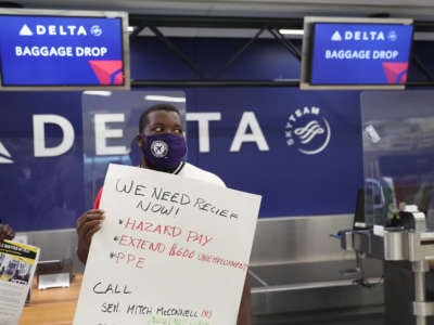 An airport worker demonstrates in front of the Delta Airlines kiosk while displaying a sign