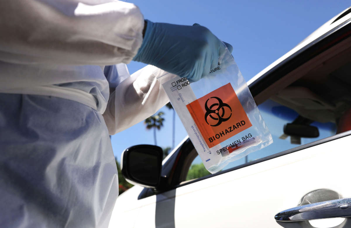 A healthcare worker prepares to hand a test kit to a motorist at a drive-in COVID-19 testing center on August 11, 2020, in Los Angeles, California.