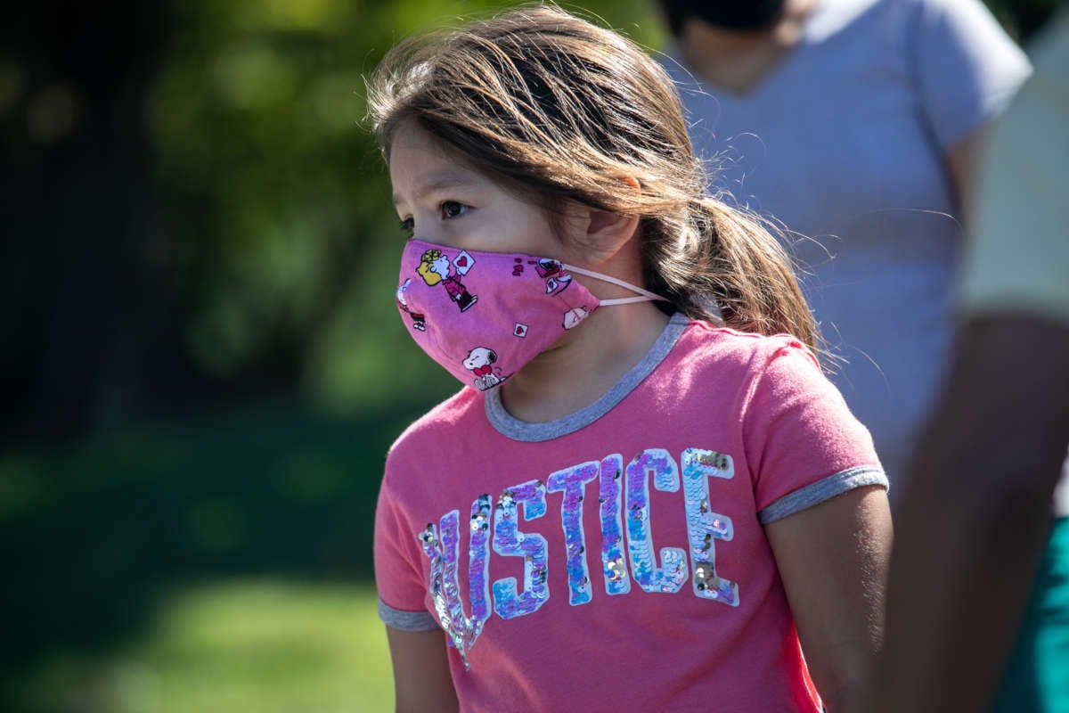 A masked girl in a shirt that reads "justice" looks onward