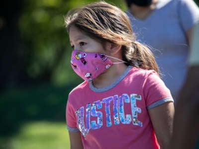 A masked girl in a shirt that reads "justice" looks onward