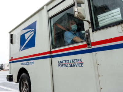 A USPS mail worker wearing a mask is seen driving between houses on August 13, 2020, in Ventnor City, New Jersey.