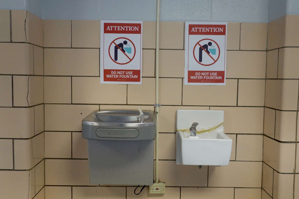 Two signs discouraging use of school water fountains are posted above two school water fountains