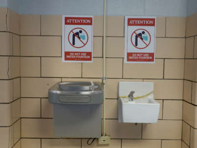 Two signs discouraging use of school water fountains are posted above two school water fountains