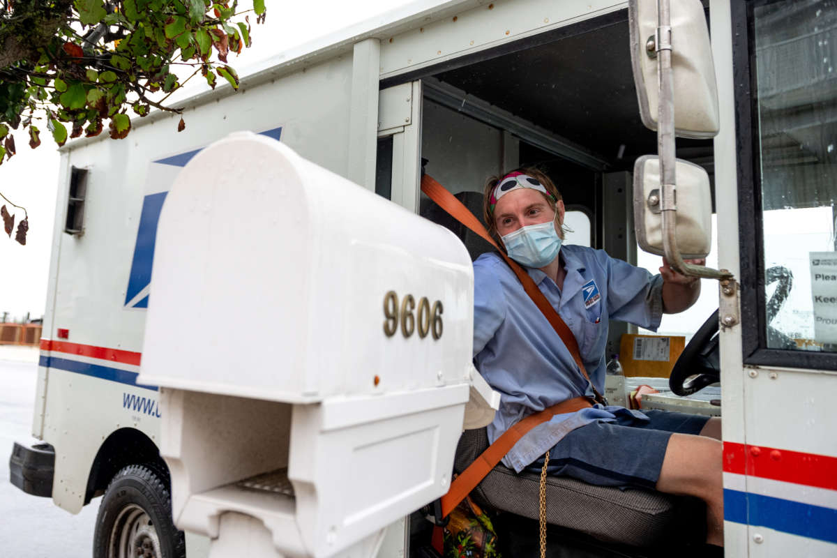 A USPS worker wearing a mask puts envelopes in a mailbox on August 13, 2020, in Ventnor City, New Jersey.
