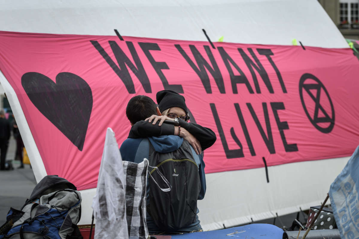 Two protesters embrace in front of a sign reading "WE WANT TO LIVE"