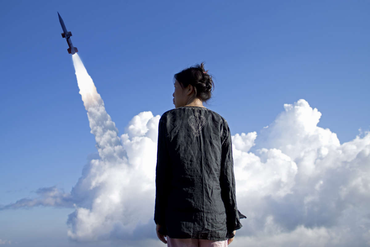 A woman stands in the foreground as a missile is launched into the sky