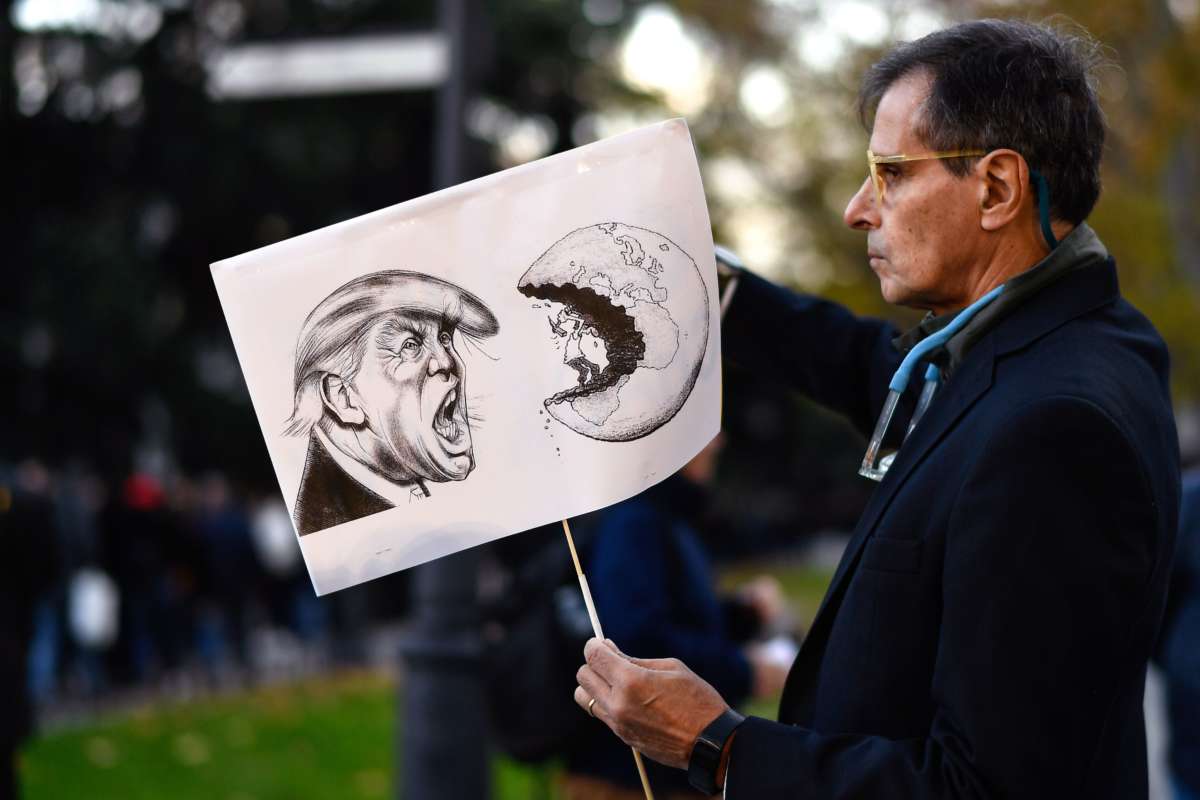 A man displays a sign with an illustration of donald trump shouting at a man mining the earth