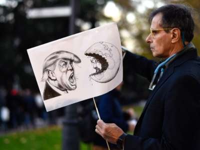 A man displays a sign with an illustration of donald trump shouting at a man mining the earth